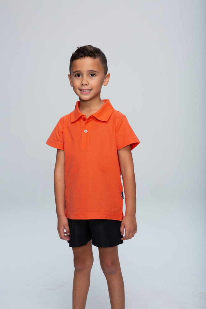 An orange polo shirt displayed on a child, paired with black shorts, standing against a neutral background.