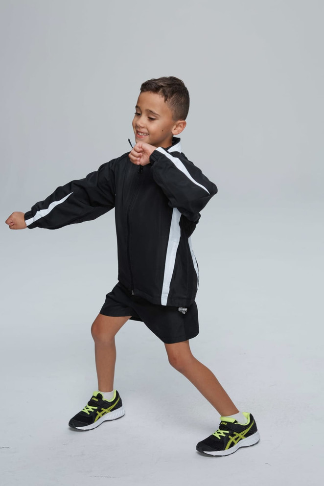 A child wearing a black track jacket with white stripes, paired with black shorts and sneakers.