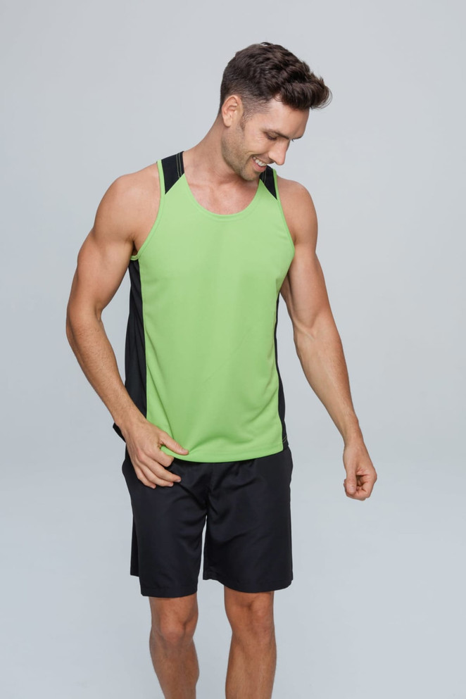 A man wearing a green and black singlet with a logo, paired with black shorts, smiling while looking down.
