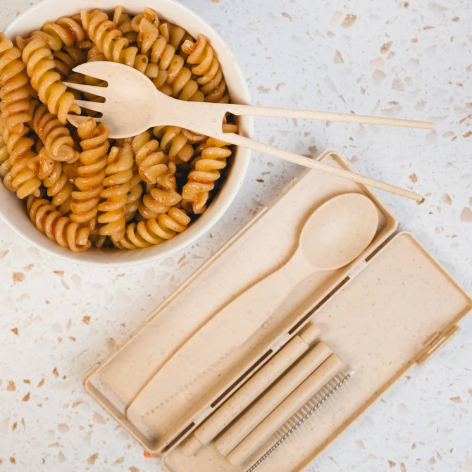 A Ramen Cutlery Set in a beige case, featuring a spoon, fork, chopsticks, and a cleaning brush, with spiral pasta in a bowl.