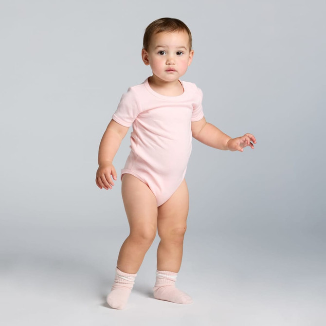 A pink organic infant one-piece with short sleeves, featuring a logo, worn by a toddler standing.
