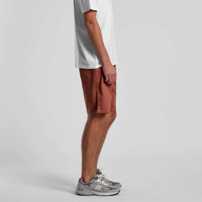 Walk shorts in a rust orange colour, featuring a logo, shown on a model from the side perspective.