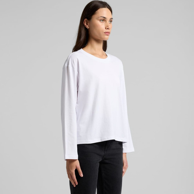 A woman wearing a white long-sleeve t-shirt, paired with black pants, standing against a plain background.