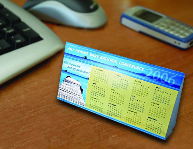 A budget desk calendar with a blue and yellow design, featuring a yearly calendar layout and a scenic image.