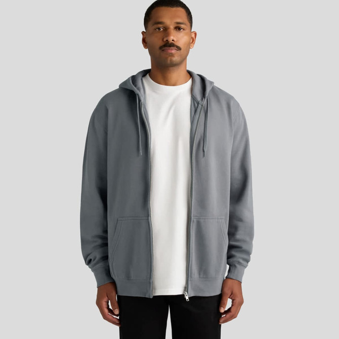 A man stands wearing a grey zip-up hoodie with a hood and kangaroo pockets. The hoodie has a logo on it.