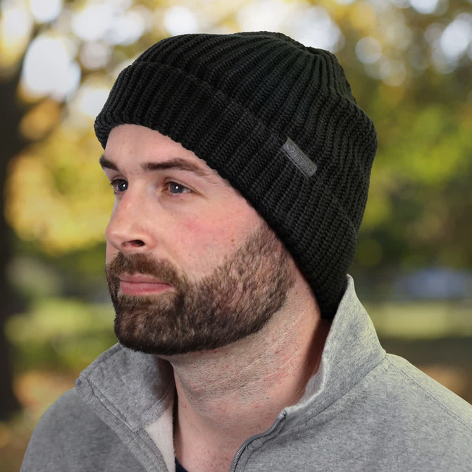 A black beanie featuring a textured knit design and a logo, worn by a man with a beard, set against a blurred outdoor background.