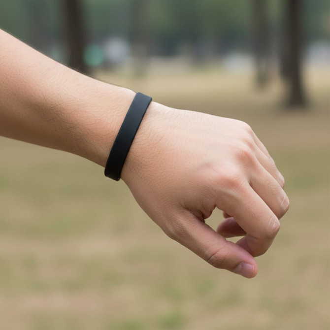 A black silicone wristband is worn on a person's wrist, set against a blurred outdoor background.