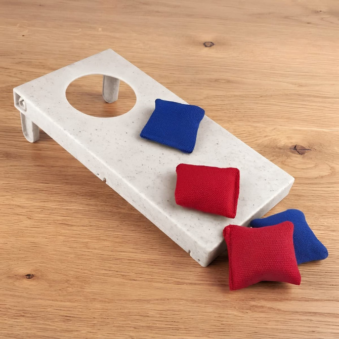 A grey cornhole board with a circular hole and four small bags, two red and two blue, on a wooden surface.