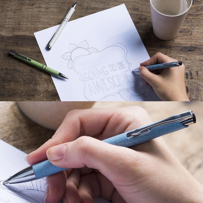 A set of Eco Pens in green, blue, and silver colours on a wooden table with paper and a cup.