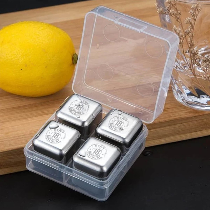 A plastic container with four stainless steel ice cubes, beside a lemon and a glass. The cubes are silver in colour.