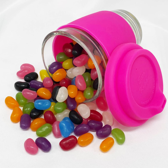 A Carlo glass coffee cup with a pink lid, filled with colourful jelly beans in various shades spilling out.
