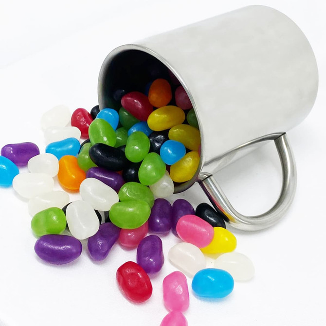 A silver mug tipped on its side, overflowing with colourful jelly beans in various shades.