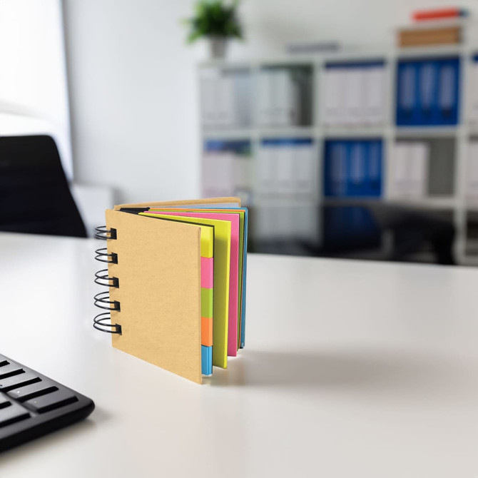 A notepad with a brown cover and colourful pages, placed on a desk in an office setting. It has a spiral binding.