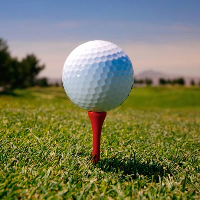A red golf tee holds a white golf ball on a grassy field under a clear sky.