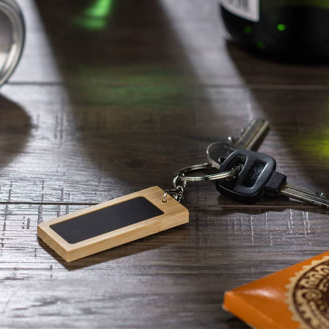 A rectangular bamboo keyring with a black panel, attached to metal keys, resting on a wooden surface.