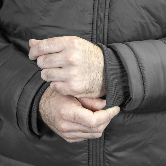 A close-up of a man's hands adjusting the cuff of a black puffer jacket, featuring a logo on the sleeve.