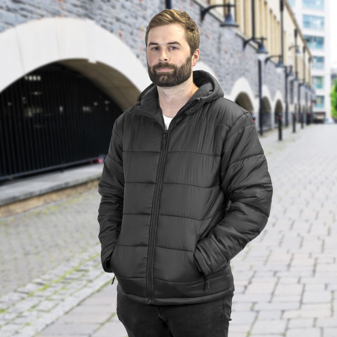 A man stands in a city street wearing a black puffer jacket with a hood, featuring side pockets and a branded logo.