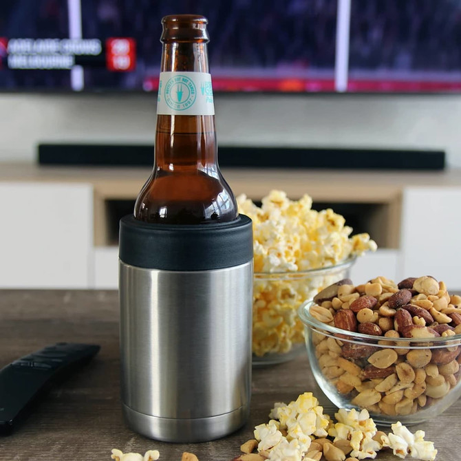 A stainless steel stubby holder with a black silicone grip, featuring a bottle inside, surrounded by snacks.