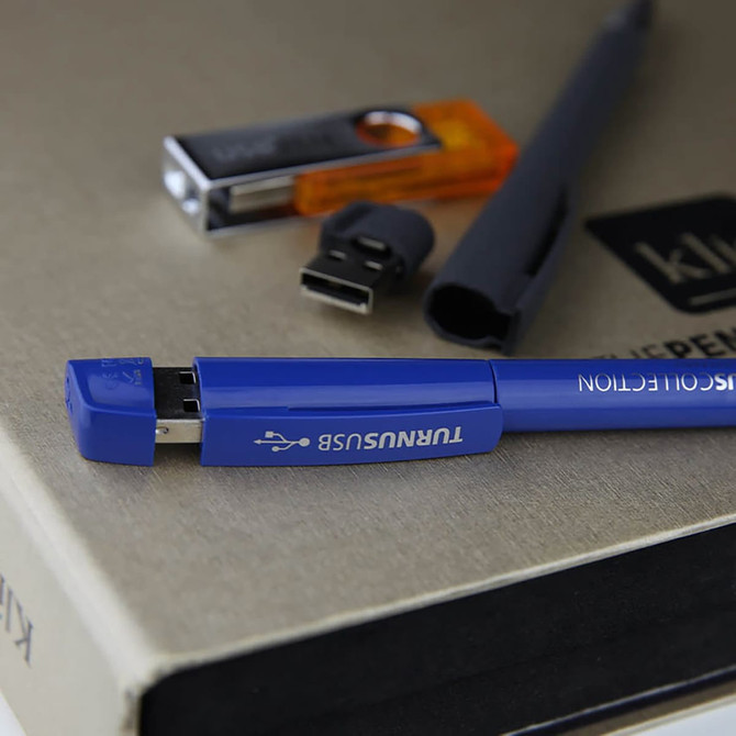A blue USB pen with a metal tip and 16GB capacity, placed alongside other flash drives on a surface.