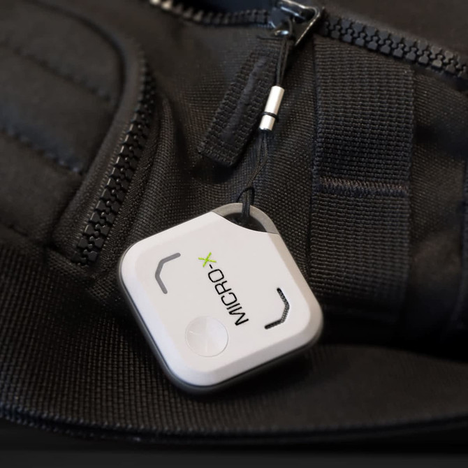 A white VibeTag Bluetooth tracker attached to a black bag zip, featuring a small logo.