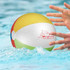 A colourful beach ball with a logo, floating in water with hands reaching for it.