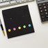 A black sticky note pad with colourful dots in pink, orange, yellow, green, and blue. Includes a logo.