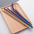 A wooden tray holds a variety of colourful stainless steel straws in gold, blue, purple, and silver.