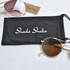 A black microfiber pouch with a logo, accompanied by brown-tinted sunglasses.