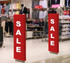 Two tall red promotional signs with bold white text displaying "SALE" in a retail store environment.
