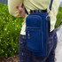 A drink bottle carrier in navy neoprene with zip pockets and an adjustable strap, worn on the side.