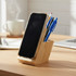 A bamboo mobile stand and pen holder in natural wood tones, featuring a smartphone and several blue and black pens.