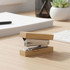 A bamboo stapler with a silver metal mechanism sits on a wooden desk, accompanied by office decor.