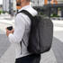 A black business computer backpack is worn on a person's back, while they hold a coffee cup in their hand.