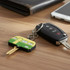 A green and yellow PVC key cover shaped like a car key, alongside a standard car key and a smartphone on a wooden surface.