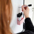 A collection of white and black Staedtler Lumocolor whiteboard markers in a holder, with a hand using one with a chisel tip.