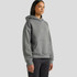 A grey hooded sweatshirt with a front pocket, featuring a relaxed fit. The model stands against a plain background.