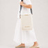 A cream cooler bag with a strap is worn across the body, featuring a logo and minimalist design.
