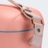 A cooler bag in soft pink with a pale strap and gold hardware, featuring a smooth, rounded design.