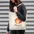 A woman holds a cream tote bag with an orange and brown logo. The bag is made from recycled cotton.