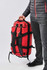 A red waterproof gear bag with shoulder straps, held by a person wearing a black puffer jacket and grey pants.