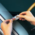 A pair of hands holding a sticker featuring a car design on a reflective surface.