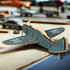 A wooden model airplane in grey, featuring intricate details and a logo, placed on a workbench with tools and materials.