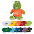A green crocodile plush toy wearing an orange shirt, accompanied by various colourful t-shirts in the background.