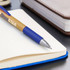 A bamboo pen with a blue grip placed on an open notebook, beside a closed leather notebook.