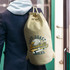 A beige canvas barrel bag with a drawstring and an eagle logo. It is slung over a person's shoulder.