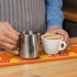 A bar runner in orange with yellow circles, holding a coffee cup and a metal milk jug on a wooden surface.