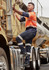 A man in an orange and navy work shirt climbs onto a truck, wearing dark blue stretch jeans with reflective stripes.