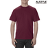 A unisex heavyweight cotton T-shirt in burgundy, featuring a logo. The model stands casually, wearing jeans.