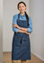 A denim apron with a fitted design, worn over a blue shirt, featuring a logo and front pockets.
