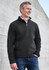 A black soft shell jacket worn by a man, featuring a zipped front and side pockets. The background is a concrete wall.